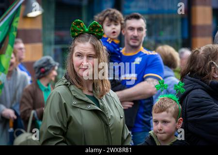 Donna con arco Shamrock in lei con suo figlio che indossa bopper alla parata del giorno di San Patrizio Foto Stock