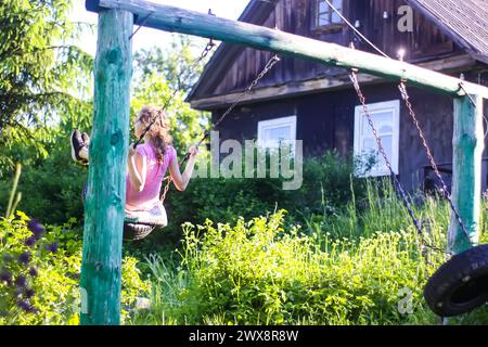 Un'infanzia felice. Durante le vacanze estive in campagna, una bambina altalena in un villaggio fatto in casa. Foto Stock