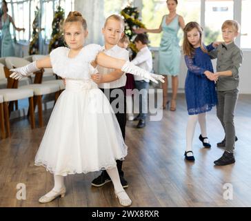 Bambini preadolescenti in abiti eleganti che praticano la danza di coppia nello studio natalizio Foto Stock