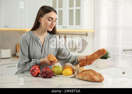 Donna con baguette e sacchetto di frutta fresca al tavolo di marmo chiaro in cucina Foto Stock