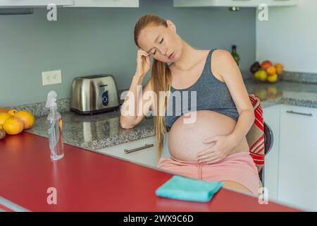 Una donna incinta stanca siede in cucina dopo la pulizia. Salute e vitalità di una donna incinta Foto Stock