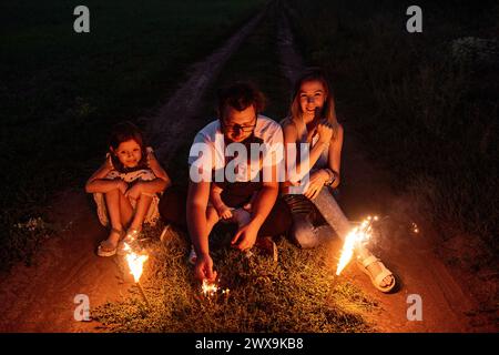 Nell'incantevole notte, una famiglia accende scintillanti su un sentiero remoto, crogiolandosi nella calda luce festosa, creando ricordi duraturi insieme. Diversi Foto Stock