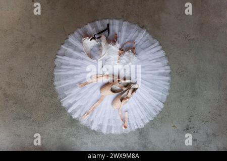 Vista dall'alto del complesso completo di balletto, con tutù, corpetto piumato e scarpe pointe, disposte su una superficie di cemento duro, evocando un senso di equilibrio Foto Stock
