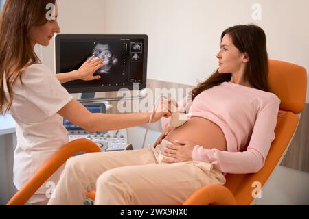 Medico donna che sposta la sonda ecografica sullo stomaco di una donna incinta Foto Stock