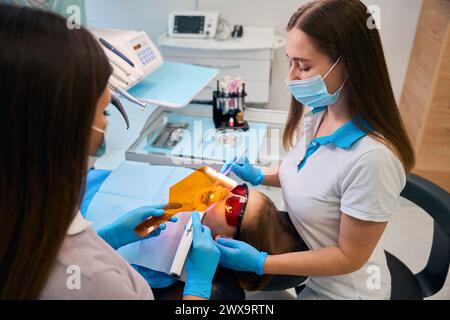La dentista donna mette un ripieno di fotopolimero su una ragazza Foto Stock