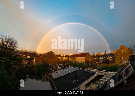 Luminoso e completo doppio arcobaleno dopo il passaggio di un temporale serale sopra un quartiere periferico di Waddinxveen, Paesi Bassi. Foto Stock