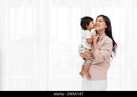 madre felice baciata dal bambino su sfondo bianco della finestra Foto Stock
