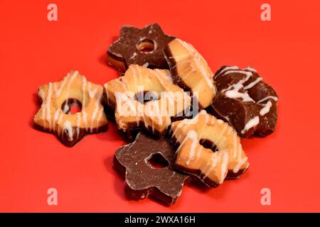 I biscotti di pasta frolla con e senza cioccolato si trovano in un mucchio su sfondo rosso, primo piano. Foto Stock