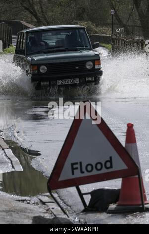 Lacock, Wiltshire, Regno Unito. 29 marzo 2024. Il fiume Avon a Lacock ha fatto scoppiare le sue sponde e ha inondato la strada dentro e fuori il villaggio. Il Consiglio è di non guidare attraverso l'acqua piena, ma la strada è percorribile se si vuole fare un tuffo. Crediti: JMF News/Alamy Live News Foto Stock