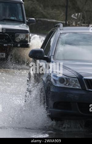 Lacock, Wiltshire, Regno Unito. 29 marzo 2024. Il fiume Avon a Lacock ha fatto scoppiare le sue sponde e ha inondato la strada dentro e fuori il villaggio. Il Consiglio è di non guidare attraverso l'acqua piena, ma la strada è percorribile se si vuole fare un tuffo. Crediti: JMF News/Alamy Live News Foto Stock