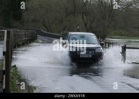 Lacock, Wiltshire, Regno Unito. 29 marzo 2024. Il fiume Avon a Lacock ha fatto scoppiare le sue sponde e ha inondato la strada dentro e fuori il villaggio. Il Consiglio è di non guidare attraverso l'acqua piena, ma la strada è percorribile se si vuole fare un tuffo. Crediti: JMF News/Alamy Live News Foto Stock