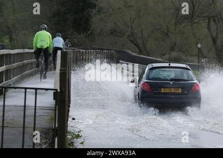 Lacock, Wiltshire, Regno Unito. 29 marzo 2024. Il fiume Avon a Lacock ha fatto scoppiare le sue sponde e ha inondato la strada dentro e fuori il villaggio. Il Consiglio è di non guidare attraverso l'acqua piena, ma la strada è percorribile se si vuole fare un tuffo. Crediti: JMF News/Alamy Live News Foto Stock