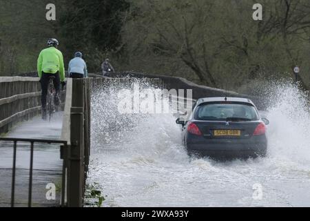 Lacock, Wiltshire, Regno Unito. 29 marzo 2024. Il fiume Avon a Lacock ha fatto scoppiare le sue sponde e ha inondato la strada dentro e fuori il villaggio. Il Consiglio è di non guidare attraverso l'acqua piena, ma la strada è percorribile se si vuole fare un tuffo. Crediti: JMF News/Alamy Live News Foto Stock