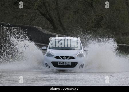 Lacock, Wiltshire, Regno Unito. 29 marzo 2024. Il fiume Avon a Lacock ha fatto scoppiare le sue sponde e ha inondato la strada dentro e fuori il villaggio. Il Consiglio è di non guidare attraverso l'acqua piena, ma la strada è percorribile se si vuole fare un tuffo. Crediti: JMF News/Alamy Live News Foto Stock