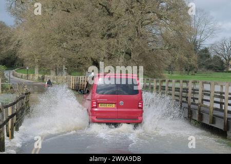 Lacock, Wiltshire, Regno Unito. 29 marzo 2024. Il fiume Avon a Lacock ha fatto scoppiare le sue sponde e ha inondato la strada dentro e fuori il villaggio. Il Consiglio è di non guidare attraverso l'acqua piena, ma la strada è percorribile se si vuole fare un tuffo. Crediti: JMF News/Alamy Live News Foto Stock