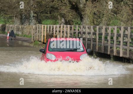 Lacock, Wiltshire, Regno Unito. 29 marzo 2024. Il fiume Avon a Lacock ha fatto scoppiare le sue sponde e ha inondato la strada dentro e fuori il villaggio. Il Consiglio è di non guidare attraverso l'acqua piena, ma la strada è percorribile se si vuole fare un tuffo. Crediti: JMF News/Alamy Live News Foto Stock