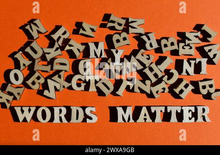Le parole contano, in lettere di legno con lettere alfabetiche casuali sopra, isolate su sfondo arancione come titolo del banner Foto Stock