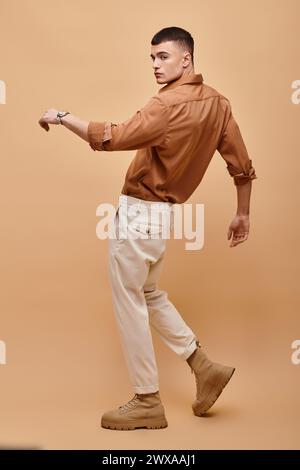 Foto a tutta lunghezza di un giovane con camicia beige, pantaloni e stivali in posa su sfondo beige Foto Stock