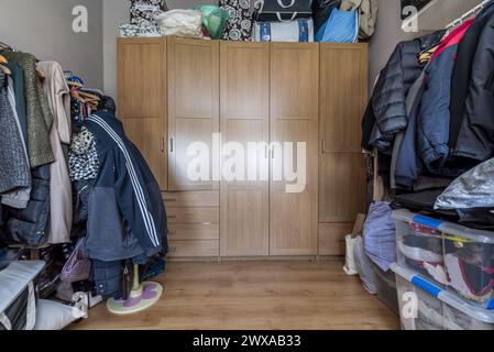 Camera da letto con un grande armadio in legno stretto e molti vestiti impilati ovunque Foto Stock