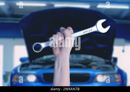 Chiave in mano davanti a una vettura blu con vano motore aperto. Pronto per l'assistenza e la manutenzione. Concetto automobilistico professionale Foto Stock