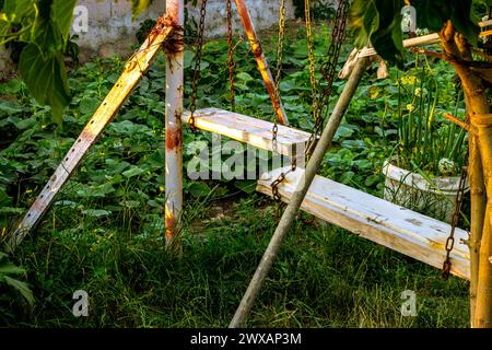 Altalena rustica adagiata in mezzo a un giardino ricoperto di vegetazione nella luce d'oro che invoca nostalgia. Foto di alta qualità Foto Stock