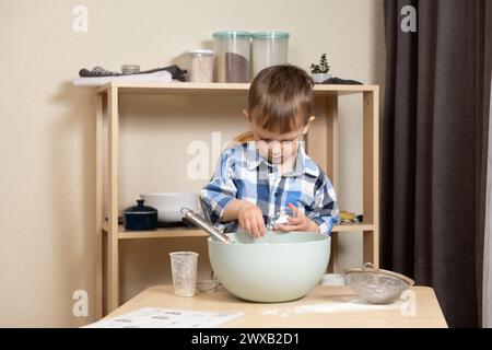 Un bambino carino che prepara l'impasto per i biscotti. I bambini in cucina Foto Stock