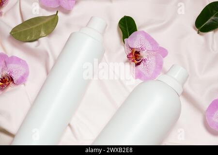 Detersivo liquido per bucato e ammorbidente per tessuti su biancheria da letto, fiori di orchidea, vista dall'alto. Foto Stock