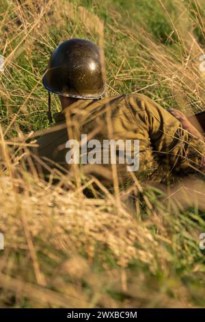 Ricostruzione storica. Un soldato di fanteria americano della seconda guerra mondiale spara nascosto nell'erba alta. Vista dal retro Foto Stock