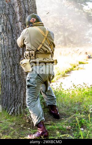 Ricostruzione storica. Un soldato di fanteria americano della seconda guerra mondiale che combatte nella foresta. Vista dal retro. Foto Stock