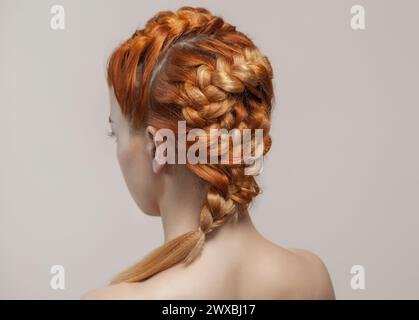 Bellissimo, con una lunga ragazza pelosa dai capelli rossi, parrucchiere intreccia una treccia, primo piano in un salone di bellezza. Cura professionale dei capelli e creazione di acconciature. Foto Stock