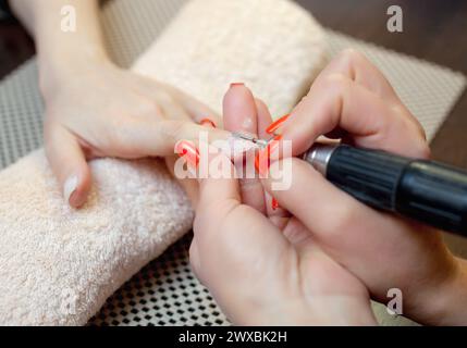 Il maestro della manicure seziona e attacca una forma di chiodo durante la procedura di estensione delle unghie con gel nel salone di bellezza. Assistenza professionale Foto Stock