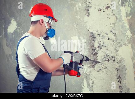 Il costruttore con attrezzatura perforatrice a martello perforatore che crea un foro nella parete nel cantiere. Foto Stock