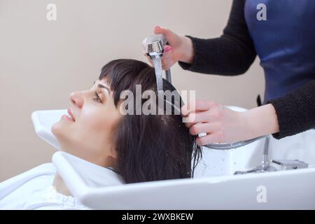 Il parrucchiere lava i capelli del cliente con lo shampoo in un salone di bellezza. Foto Stock