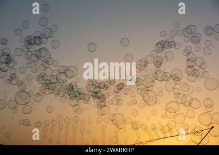 Molte bolle di sapone colorate fluttuano nel cielo arancione al tramonto con il bastoncino di sapone Foto Stock