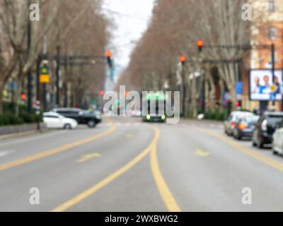 Una vivace e moderna strada cittadina caratterizzata da un autobus verde, automobili e semafori in una sfocatura che suggerisce movimento e attività urbana. Foto Stock
