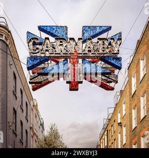 La scintillante bandiera Union sopra Carnaby Street è un simbolo della cultura e della moda britannica, con i suoi dischi a specchio che riflettono l'atmosfera vibrante della zona. Foto Stock