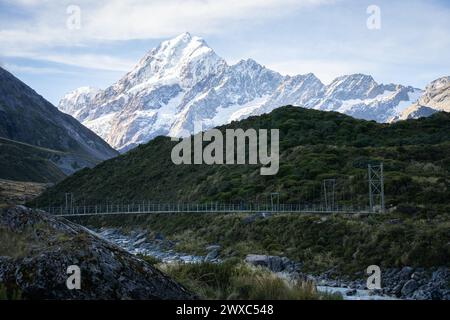 Ponte sospeso che conduce attraverso la valle alpina con un'enorme montagna innevata alle sue spalle, Mt Cook, nuova Zelanda. Foto Stock