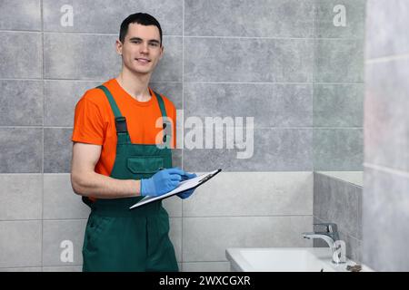 Giovane idraulico che scrive i risultati dell'esame del lavandino in bagno Foto Stock