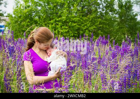 Madre e bambino nel parco soleggiato. Mamma e bambino nel giardino estivo. Donna che tiene in braccio un bambino appena nato. Mamma attiva dopo la nascita. Foto Stock