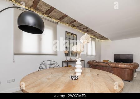 Soggiorno con divano letto modello Chester rivestito in pelle marrone, tavolo circolare in legno di design industriale e lampada in metallo nero Foto Stock