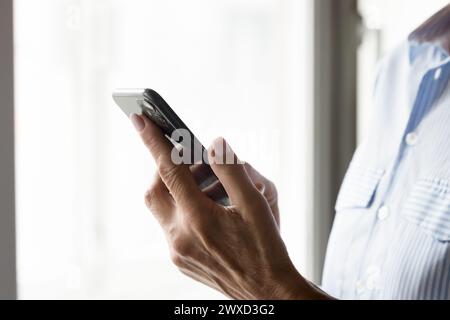 Mani di donne mature che tengono lo smartphone nero contro la finestra Foto Stock