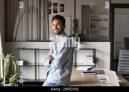 Felice fiducioso bello giovane uomo d'affari indiano in posa in ufficio Foto Stock