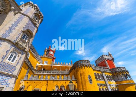 Ampia vista esterna del Palácio da pena con pareti di colore giallo e rosso e mosaici sulle pareti e le mura fortificate, sotto un cielo azzurro e soleggiato. Sintra Foto Stock