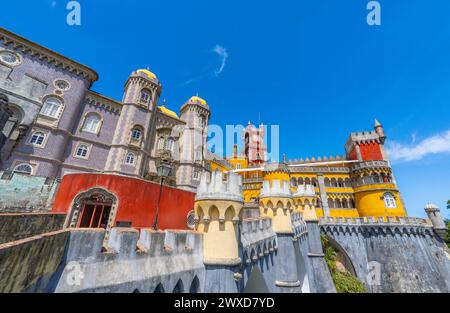 Ampia vista esterna del Palácio da pena con pareti di colore giallo e rosso e mosaici sulle pareti e le mura fortificate, sotto un cielo azzurro e soleggiato. Sintra Foto Stock