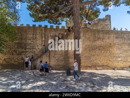 Turisti e famiglie che salgono le scale delle mura di Lisbona George's Castle all'ombra di un pino in una giornata di sole. Foto Stock