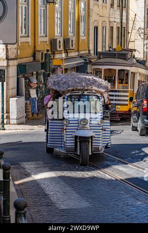 Tuk tuk tuk tuk o Autorickshaw bianco a righe blu, che sale su una strada acciottolata con binari e rotaie del tram nel quartiere di Alfama Foto Stock