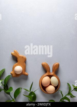 Uova di Pasqua biologiche di colori naturali in piatti a forma di coniglio e carota e ramoscelli verdi di Ruscus sullo sfondo grigio neutro. Pasqua ca Foto Stock