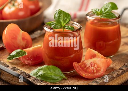 Due bicchieri di succo di pomodoro con foglie di basilico e affettare i pomodori su un vassoio di legno Foto Stock