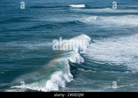 Onde oceaniche turchesi giganti si schiantano sulla superficie dell'acqua formando un arcobaleno Foto Stock