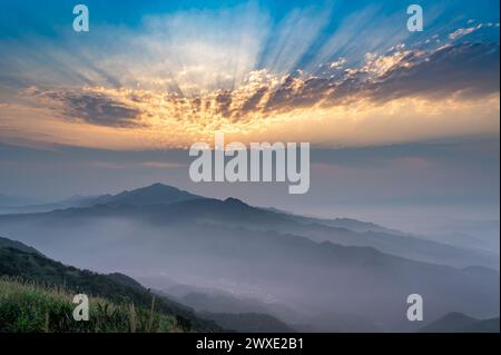 Il sole al tramonto proietta un velo di nebbia in vivaci sfumature arancioni, creando un ampio arazzo di colore sulla montagna. Buyan Pavilion, New Taipei City. Foto Stock